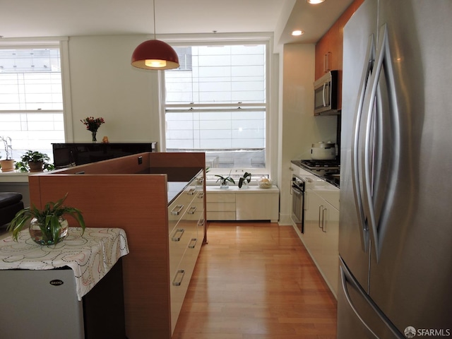 kitchen with light wood-type flooring, appliances with stainless steel finishes, hanging light fixtures, and a healthy amount of sunlight