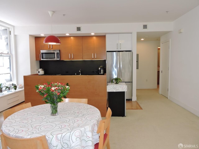 kitchen featuring white cabinetry, backsplash, stainless steel appliances, decorative light fixtures, and light carpet