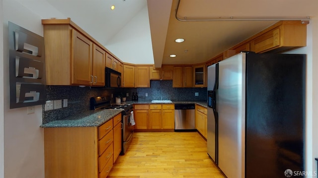 kitchen with dark stone counters, light hardwood / wood-style floors, tasteful backsplash, vaulted ceiling, and black appliances