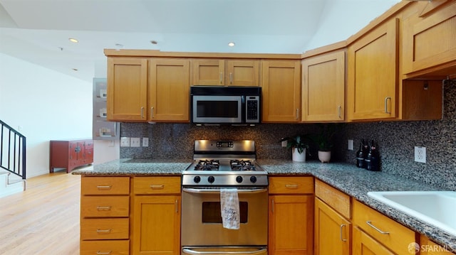 kitchen featuring stainless steel appliances, dark stone countertops, light hardwood / wood-style floors, and tasteful backsplash