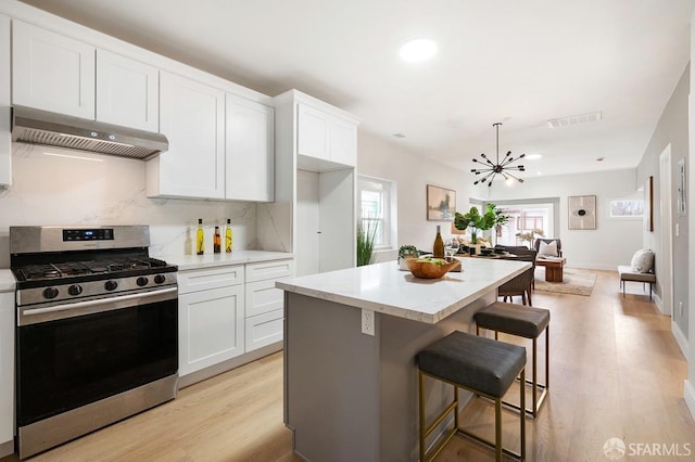 kitchen with a center island, ventilation hood, stainless steel range with gas cooktop, and white cabinetry