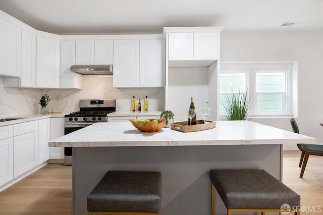 kitchen with light hardwood / wood-style flooring, gas range, tasteful backsplash, light stone counters, and white cabinetry