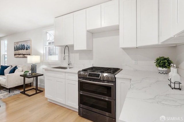 kitchen with light stone countertops, white cabinetry, sink, double oven range, and light wood-type flooring