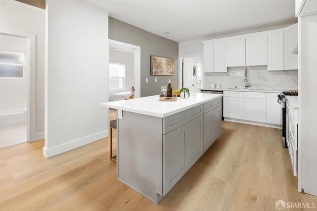 kitchen with backsplash, a center island, sink, stainless steel gas stove, and white cabinetry