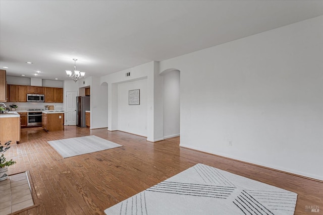 living room with arched walkways, baseboards, an inviting chandelier, and wood finished floors