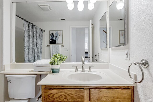 full bath with a shower with curtain, visible vents, vanity, and toilet