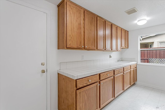 kitchen featuring a textured ceiling, a sink, visible vents, baseboards, and light countertops