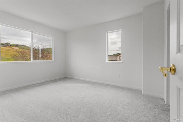 empty room with a wealth of natural light, light colored carpet, and baseboards