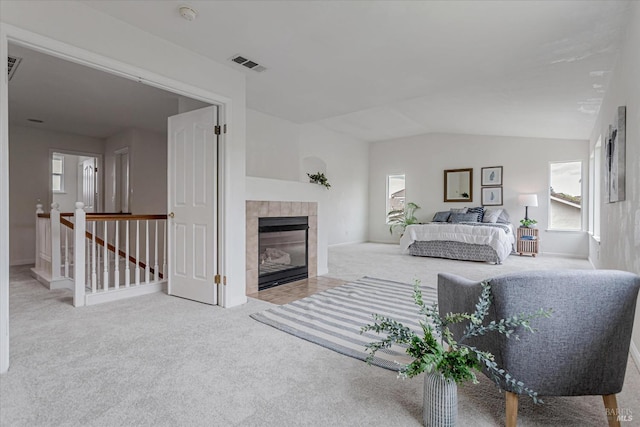 carpeted bedroom with vaulted ceiling, a tile fireplace, and visible vents