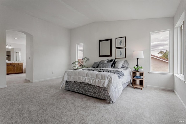 bedroom with light carpet, baseboards, arched walkways, lofted ceiling, and ensuite bath