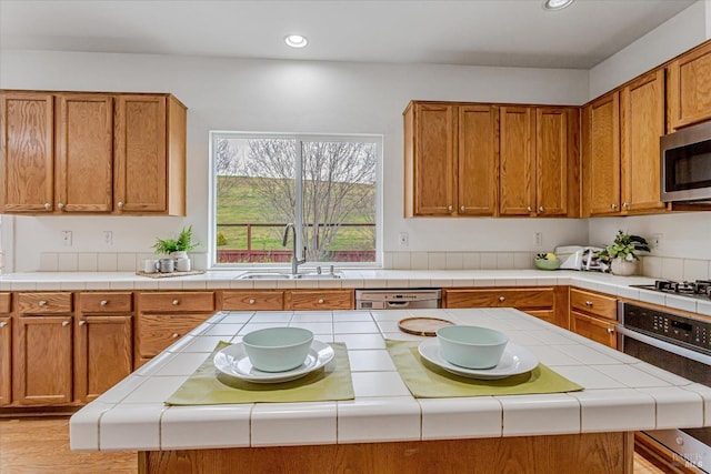 kitchen with a center island, stainless steel appliances, recessed lighting, brown cabinetry, and a sink