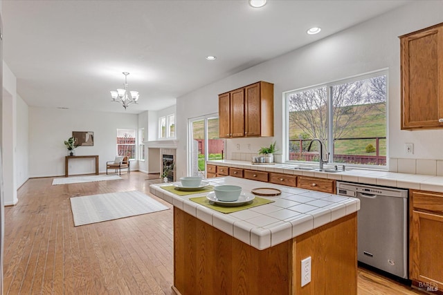 kitchen featuring tile counters, brown cabinets, open floor plan, stainless steel dishwasher, and a sink