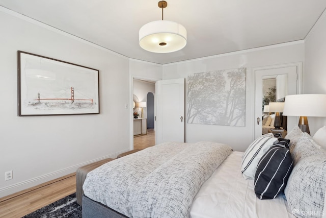 bedroom with arched walkways, light wood-style flooring, crown molding, and baseboards