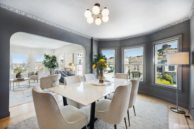 dining room with arched walkways, a notable chandelier, light wood-type flooring, and crown molding