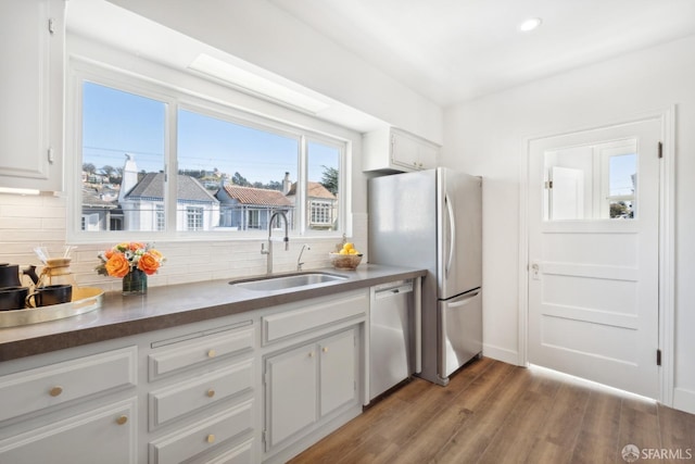 kitchen with wood finished floors, stainless steel appliances, decorative backsplash, a sink, and white cabinetry