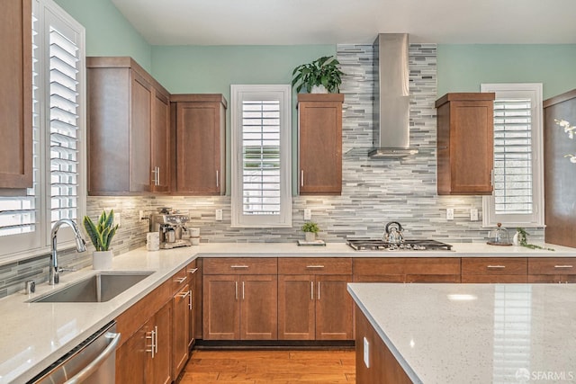 kitchen with tasteful backsplash, wall chimney exhaust hood, light stone counters, appliances with stainless steel finishes, and a sink