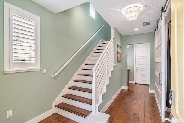 stairway with a barn door, visible vents, baseboards, wood finished floors, and a chandelier