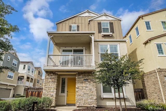 view of front facade with a balcony, fence, stone siding, stucco siding, and board and batten siding