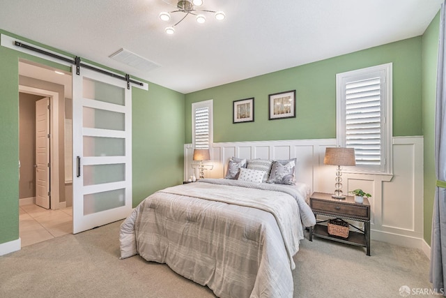 bedroom featuring a barn door, tile patterned flooring, a wainscoted wall, visible vents, and carpet