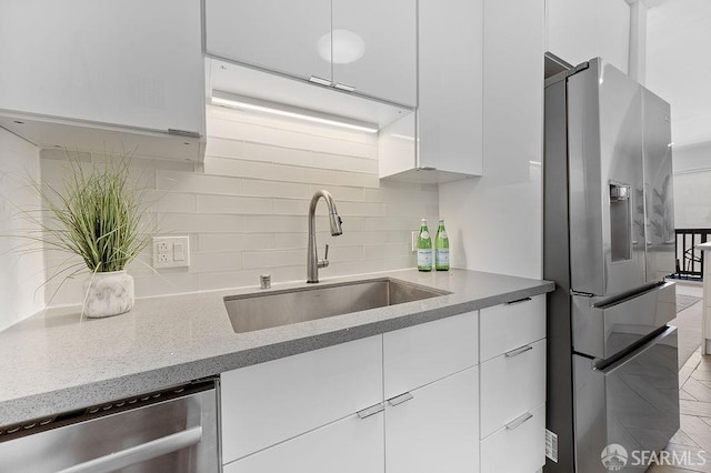 kitchen featuring appliances with stainless steel finishes, a sink, decorative backsplash, and white cabinetry