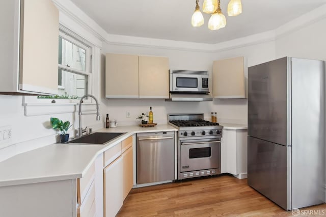 kitchen featuring appliances with stainless steel finishes, sink, light wood-type flooring, hanging light fixtures, and an inviting chandelier