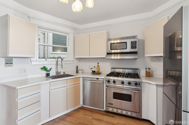 kitchen with appliances with stainless steel finishes, sink, an inviting chandelier, and light wood-type flooring