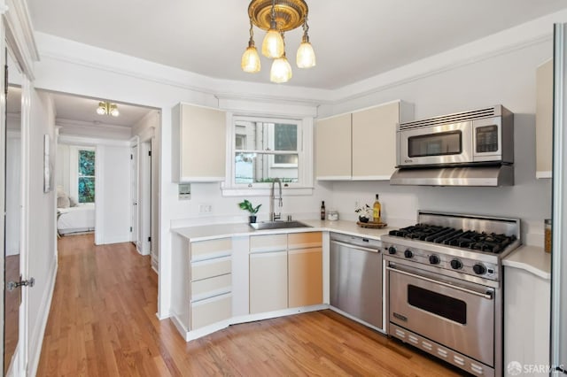 kitchen with pendant lighting, sink, stainless steel appliances, ornamental molding, and light wood-type flooring