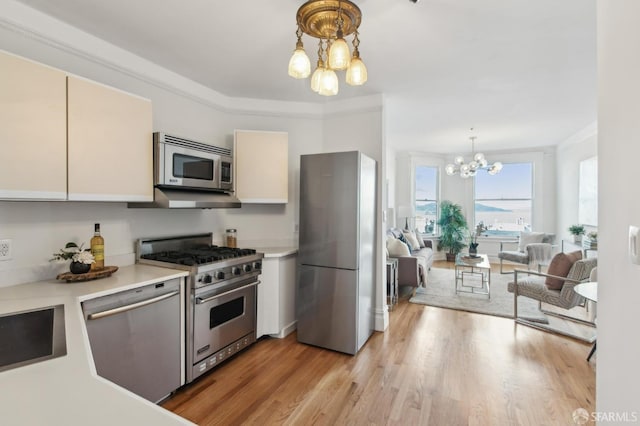 kitchen featuring an inviting chandelier, crown molding, hanging light fixtures, light wood-type flooring, and stainless steel appliances