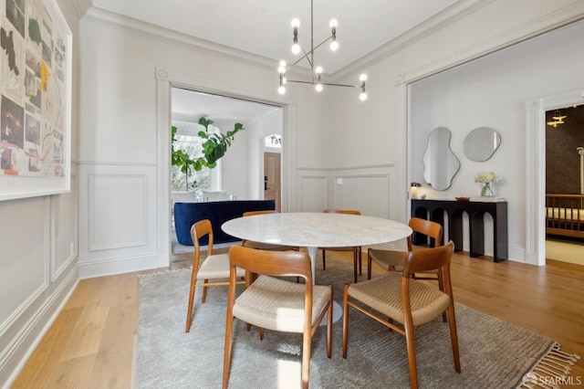dining area featuring crown molding, a notable chandelier, light wood-style flooring, and a decorative wall