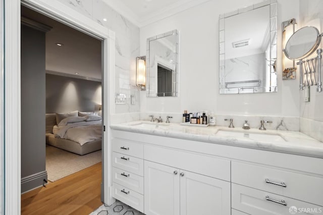 ensuite bathroom with a sink, connected bathroom, wood finished floors, and ornamental molding
