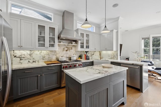kitchen featuring wall chimney range hood, appliances with stainless steel finishes, gray cabinetry, and light wood finished floors