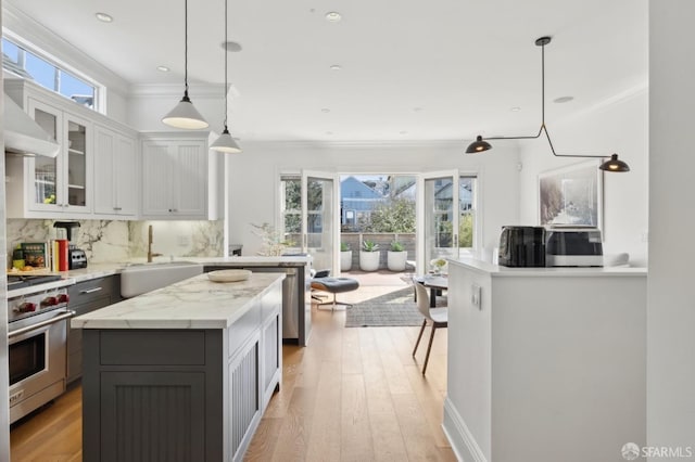 kitchen with crown molding, decorative backsplash, a sink, light wood finished floors, and appliances with stainless steel finishes