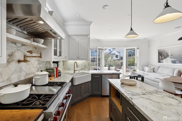 kitchen featuring appliances with stainless steel finishes, wood finished floors, a sink, ornamental molding, and wall chimney exhaust hood