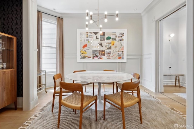 dining space featuring an inviting chandelier, ornamental molding, wainscoting, and a decorative wall