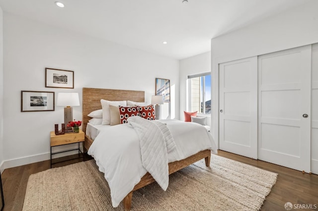 bedroom with recessed lighting, wood finished floors, baseboards, and a closet