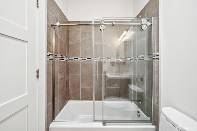 bathroom featuring toilet and bath / shower combo with glass door