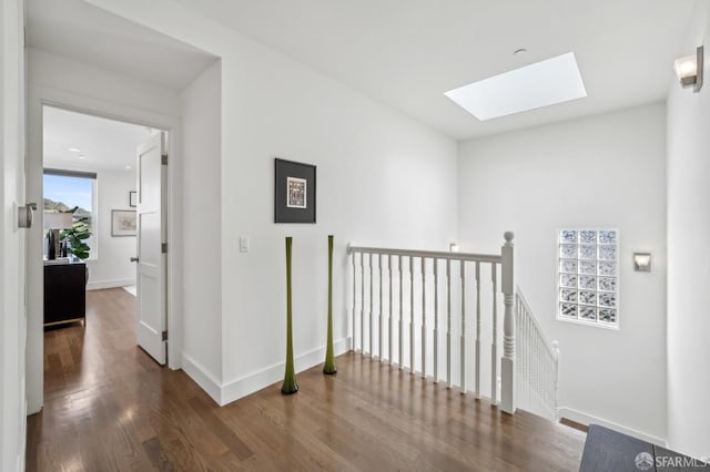 hall with wood finished floors, a skylight, an upstairs landing, and baseboards