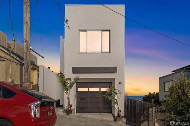 modern home featuring fence, a garage, driveway, and stucco siding