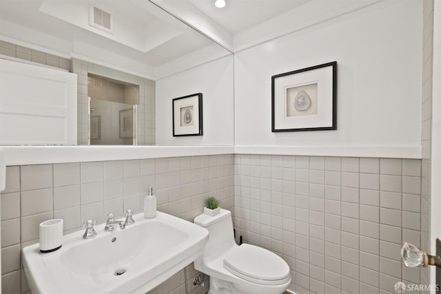 bathroom featuring a sink, visible vents, toilet, and tile walls