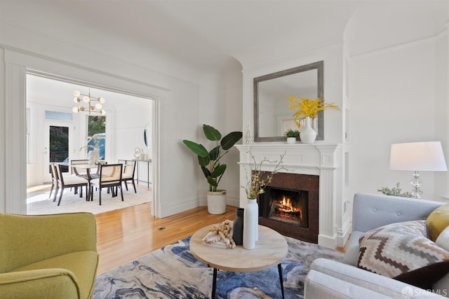 living area with a premium fireplace, a notable chandelier, baseboards, and wood finished floors