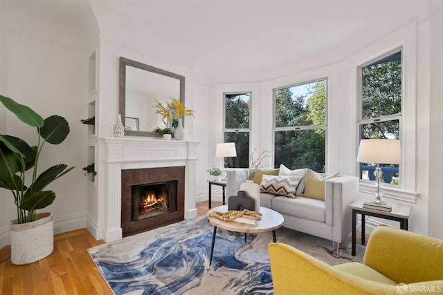 living room featuring baseboards, a warm lit fireplace, and wood finished floors