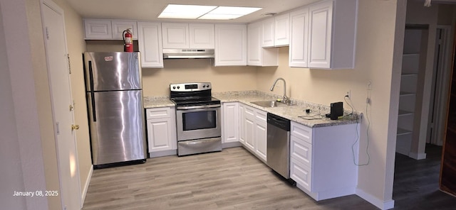 kitchen featuring sink, white cabinetry, light stone counters, light hardwood / wood-style flooring, and appliances with stainless steel finishes