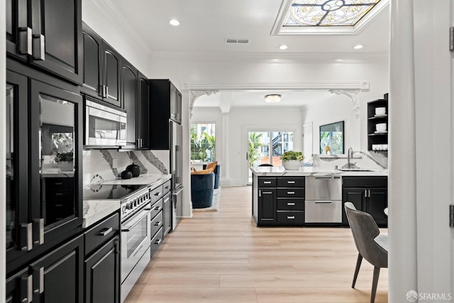 kitchen featuring light wood-style flooring, crown molding, high quality appliances, dark cabinets, and backsplash