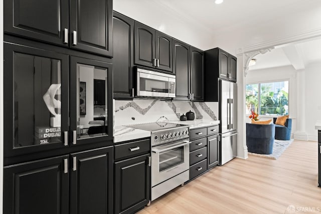 kitchen featuring decorative backsplash, high end appliances, ornamental molding, light stone counters, and light hardwood / wood-style floors