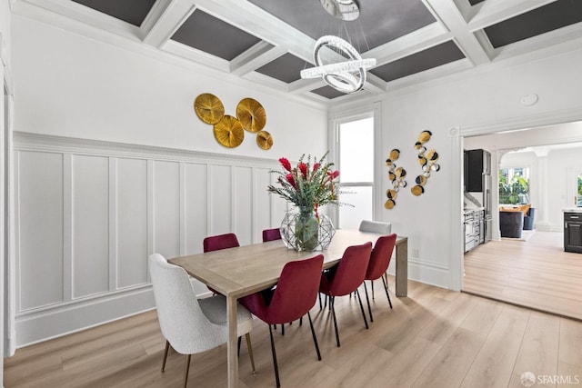 dining area with beamed ceiling, a chandelier, ornamental molding, coffered ceiling, and light hardwood / wood-style floors