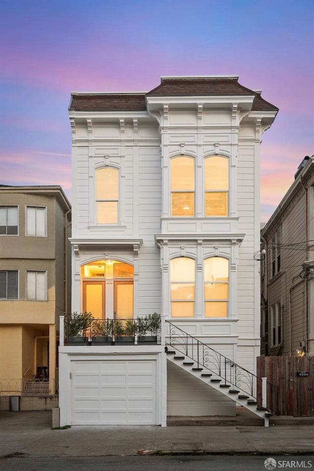 italianate home featuring a garage, roof with shingles, driveway, and fence