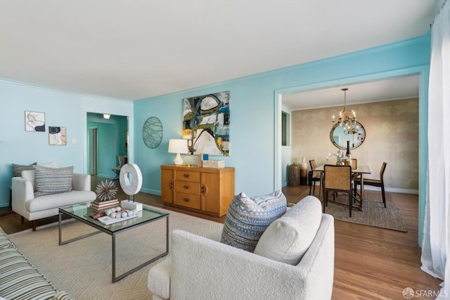 living room featuring baseboards, ornamental molding, wood finished floors, and a notable chandelier