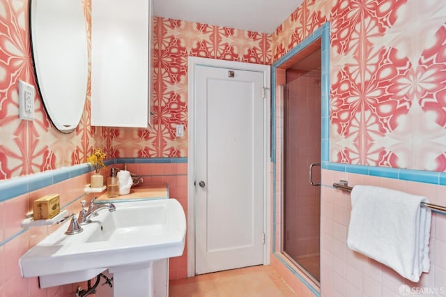 full bath featuring a sink, tile walls, wainscoting, a stall shower, and wallpapered walls