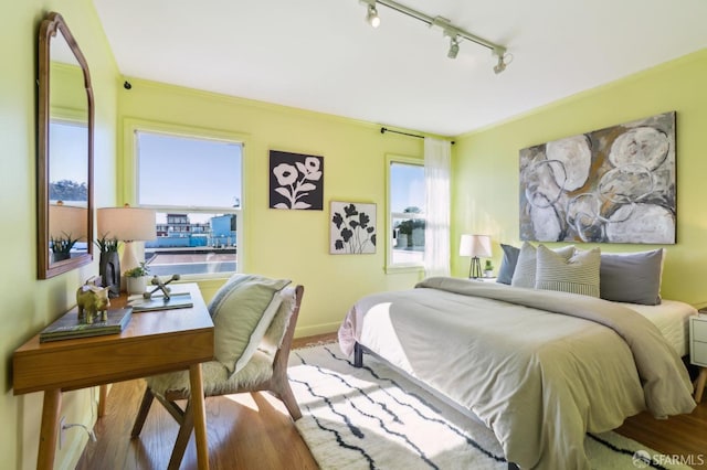 bedroom with track lighting, baseboards, and wood finished floors