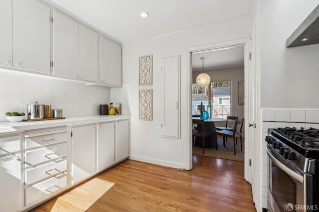 kitchen featuring light wood finished floors, stainless steel gas range oven, white cabinets, decorative backsplash, and light countertops